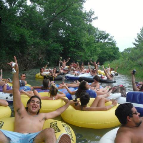 A large group of people cheering for the camera as they float down the river