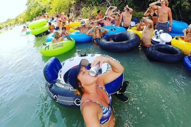 A group of people shotgunning beers while floating down the San Marcos River