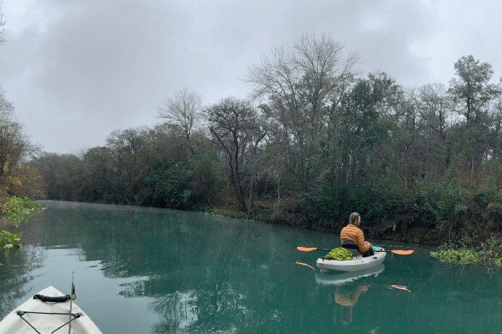 a man riding on the back of a boat next to a lake
